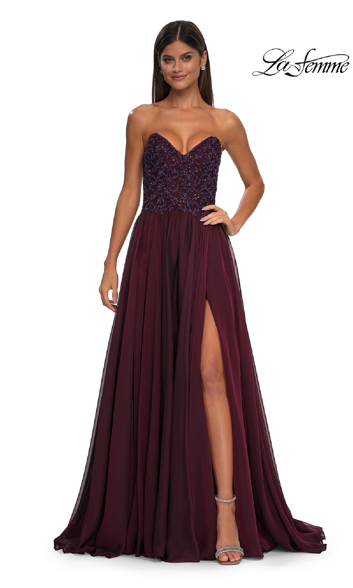 A woman wears the La Femme 32804 strapless long a-line prom dress in burgundy, showcasing a beaded bodice and thigh-high slit, as she stands against a white background.